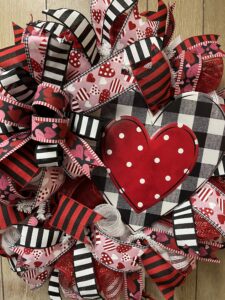 Deco mesh valentine wreath with a metal heart sign of black and white buffalo plaid and red heart with white polka dots. Valentines day ribbons with red and pink hearts on black ribbon, black and white striped ribbon, black and red striped ribbon. pink ribbon with red and white hearts.