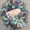 picture of a spring deco mesh wreath with hello spring sign and beautiful spring colored ribbons of purple, teal and whit with flowers