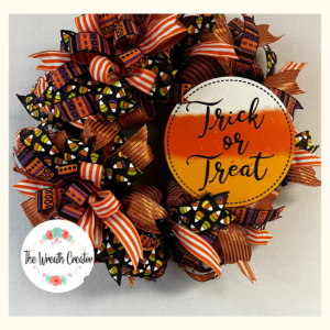 halloween deco mesh wreath with white, orange and yellow trick or treat sign, orange and white striped ribbon, candy corn on black ribbon, purple and orange squiggly ribbon and orange sparkle ribbon with a bow made out of all those ribbons.