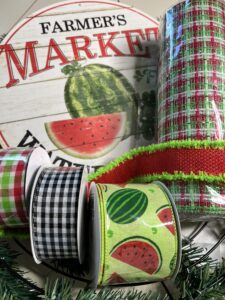 picture of wreath supplies with a farmers market watermelon, red and green deco mesh, watermelon ribbon, red and green plaid ribbon,red and green ribbon and a black and white gingham plaid ribbon.