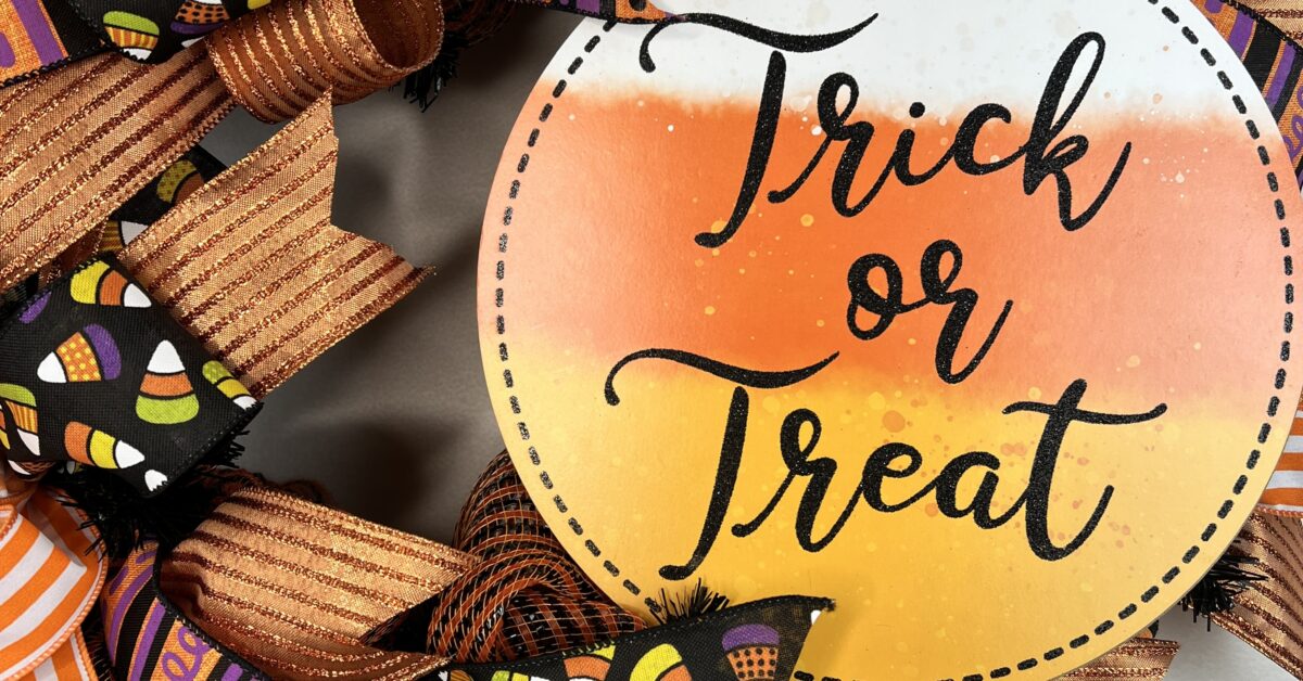 trick or treat halloween wreath with orange and purple ribbons, candy corn ribbons and a large trick or treat sign. This wreath has orange deco mesh as its base on a wire wreath frame. two big beautiful matching ribbon bows adorn this wreath.