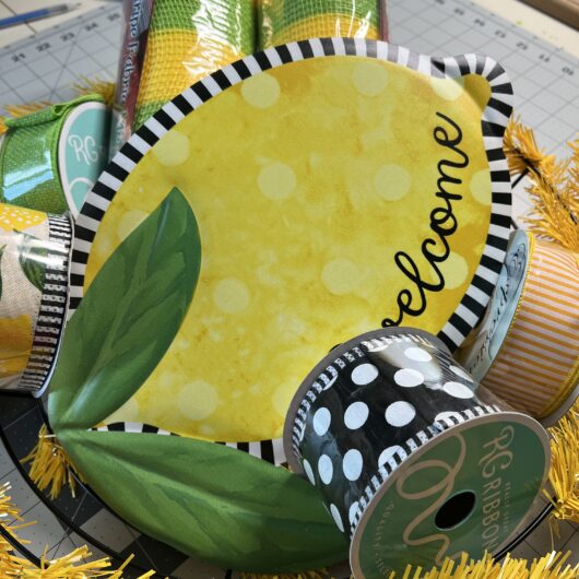 picture of wreath kit, that includes a lemon welcome sign, lemon designed ribbon, blak with white polka dot ribbon, yellow and white striped ribbon, lime green ribbon, rolls of lime and yellow striped deco mesh and a yellow wreath form.