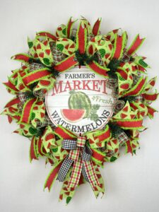 beautiful summer deco mesh wreath with farmer's market watermelon sign, coordinating watermelon ribbons, green and red ribbons, plaid ribbons and matchin bow on a background of red, green and white deeco mesh.