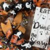 halloween wreath with a ghost sign reading Eat, drink and be scary, ghostly ribbons, orange and black with spider ribbons and black with skulls adorn this wreath, the base of this wreath is orange and white striped deco mesh and two big beautiful bows in the matching ribbons are attached.