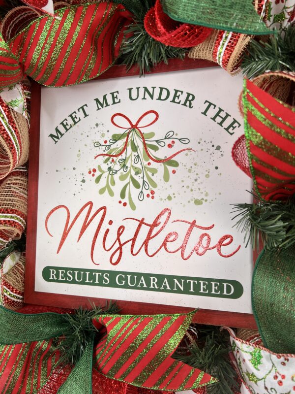 Christmas wreath with Meet me under the mistletoe sign placed in the middle of the wreath,red, green and white glittered ribbons, mistletoe ribbon with a large bow with the same ribbons adorn this wreath