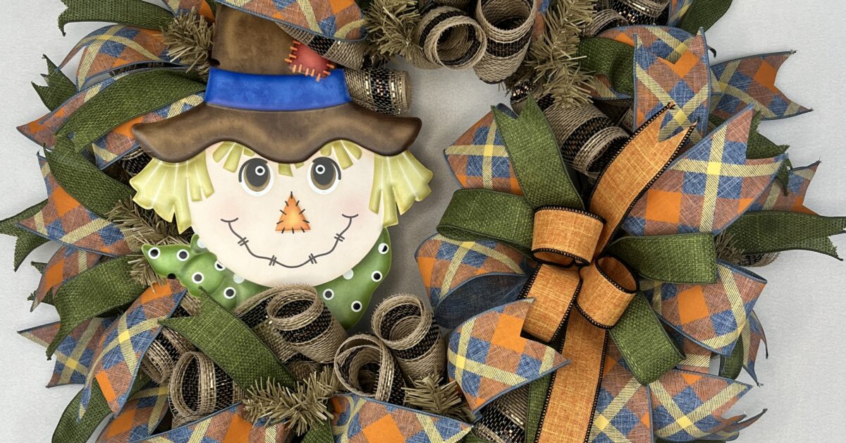 fall scarecrow wreath with a cute scarecrow face sign. Fall moss green, orange and fall plaid colored ribbons. one large cascading ribbon bow of the same ribbons adorn this wreath. All on a burlap and brown with a little metallic copper stripe deco mesh base.