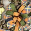 fall scarecrow wreath with a cute scarecrow face sign. Fall moss green, orange and fall plaid colored ribbons. one large cascading ribbon bow of the same ribbons adorn this wreath. All on a burlap and brown with a little metallic copper stripe deco mesh base.