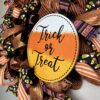 trick or treat halloween wreath with orange and purple ribbons, candy corn ribbons and a large trick or treat sign. This wreath has orange deco mesh as its base on a wire wreath frame. two big beautiful matching ribbon bows adorn this wreath.