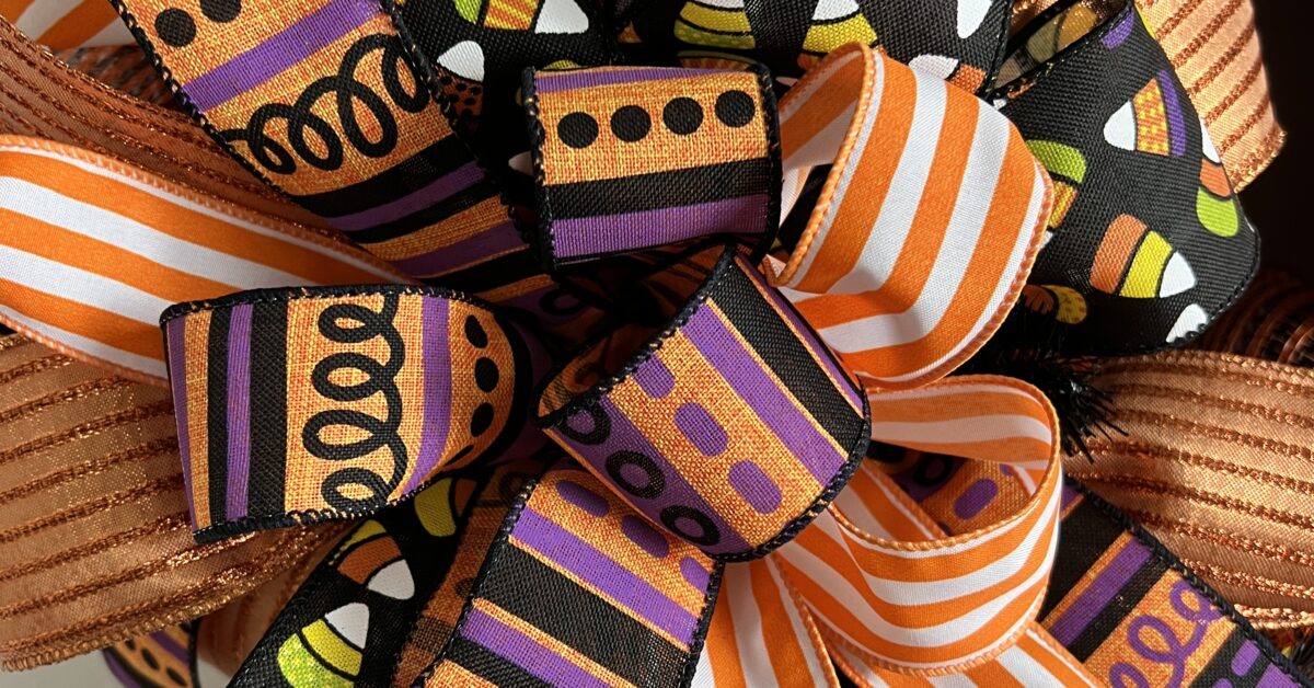 trick or treat halloween wreath with orange and purple ribbons, candy corn ribbons and a large trick or treat sign. This wreath has orange deco mesh as its base on a wire wreath frame. two big beautiful matching ribbon bows adorn this wreath.