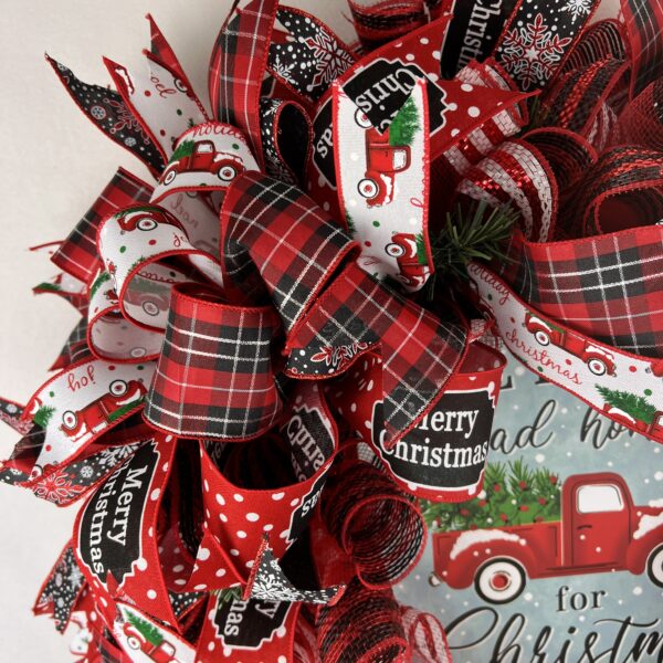 christmas holiday wreath with all roads lead home for christmas sign, sign ahs red truck with christmas tree in the back, red plaid ribbons, merry christmas ribbon, snowflake ribbon, red truck ribbons, red and white border deco mesh is the base, a bow adorns the wreath in matching ribbons