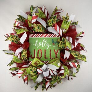 Christmas holiday wreath with red and green Holly Jolly sign in the center of the wreath, with santa ho ho ho ribbons, mistle toe ribbons, red and white stripped ribbon, white ribbon, a bow of matching ribbons is under the sign, red deco mesh is the base for this wreath