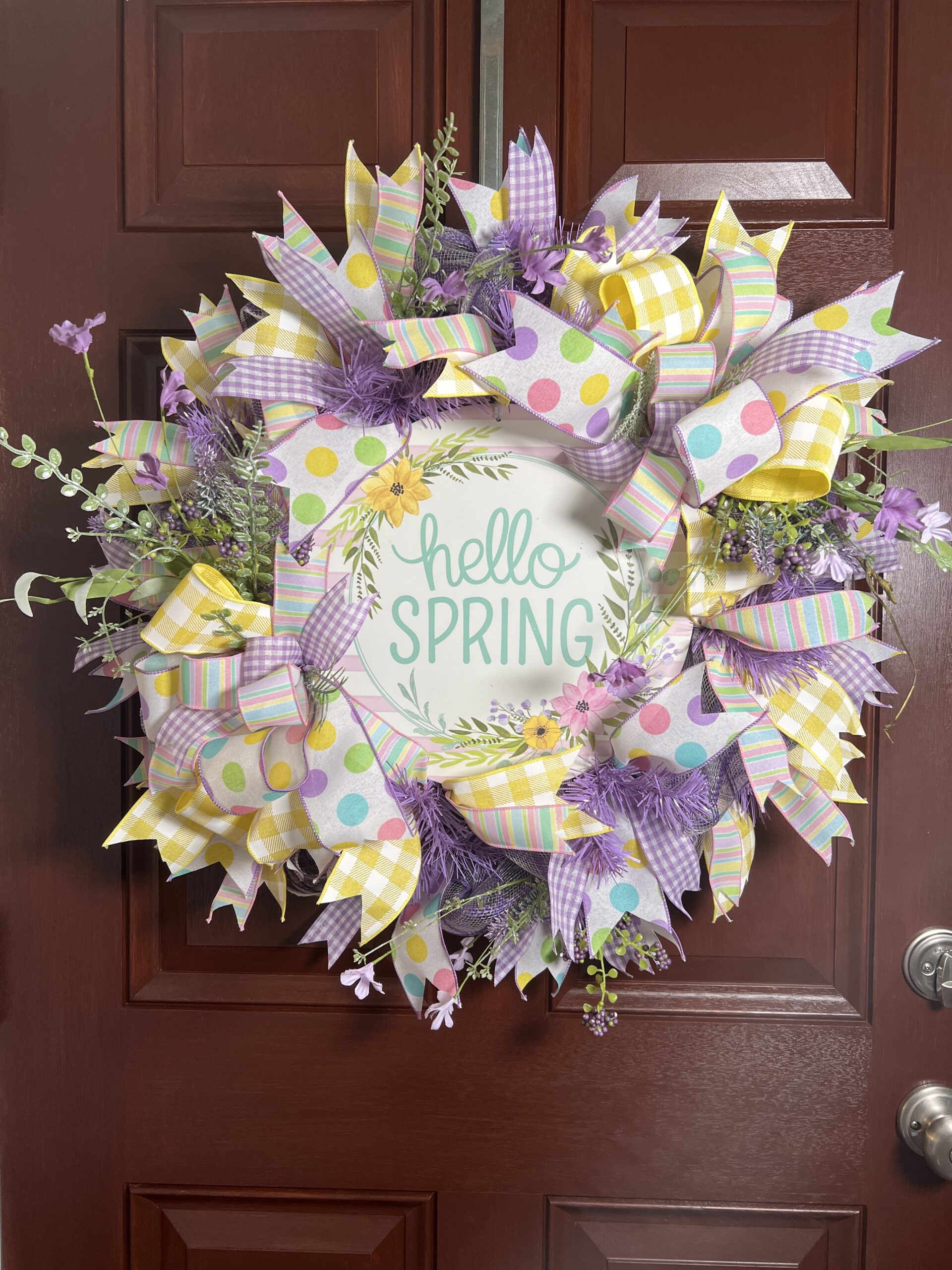 spring deco mesh wreath, hello spring sign, yellow and white plaid ribbon, purple and white gingham ribbon, spring colored polka dot ribbon, pastel spring colored striped ribbon, lavender and white plaid deco mesh base, lavender spring flowers